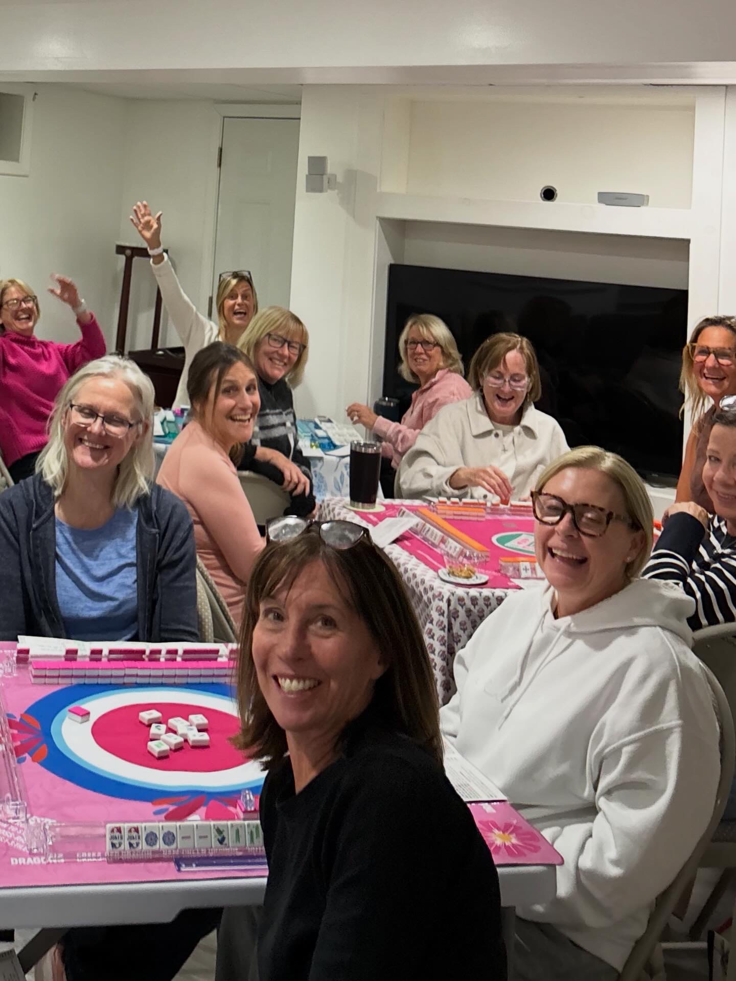 A full room of players laughing around mahjong tables at league night